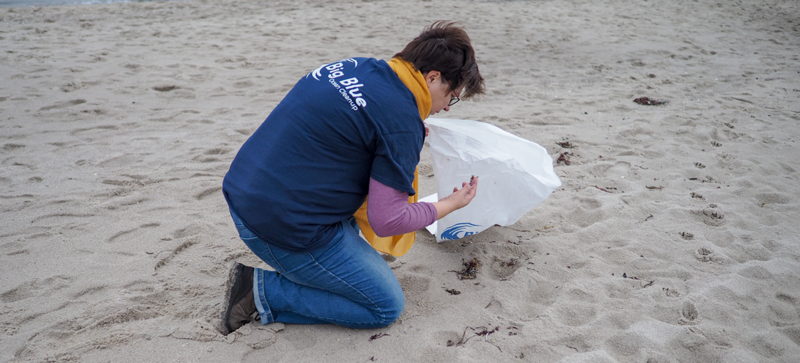Una mujer en la playa con una bolsa de basura