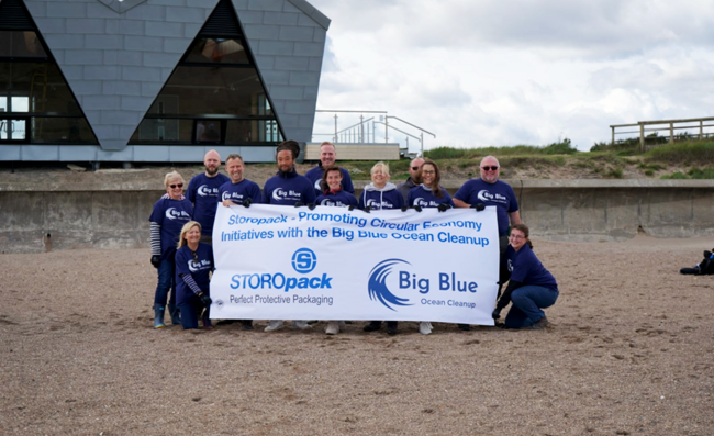 Varias personas posan para una foto de grupo en la playa sosteniendo una pancarta de Big Blue Ocean Cleanup