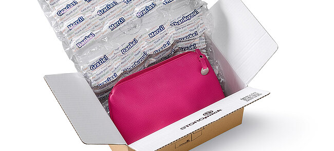 Una caja de cartón que contiene una bolsa rosa y acolchado de aire con un diseño impreso