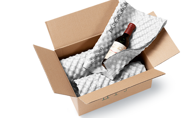 Una caja de cartón con botellas de vino envueltas en hojas de papel blanco de burbujas