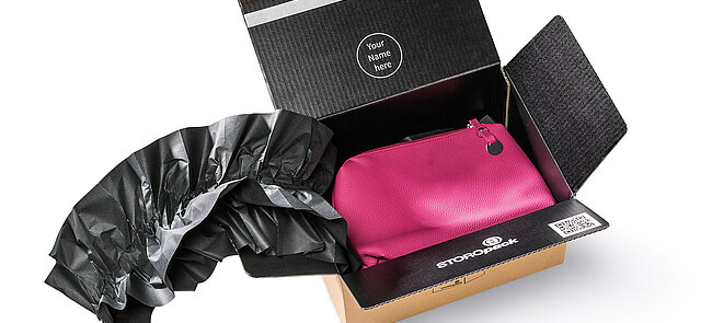 Una caja de cartón que contiene una bolsa rosa y almohadillados de papel negro
