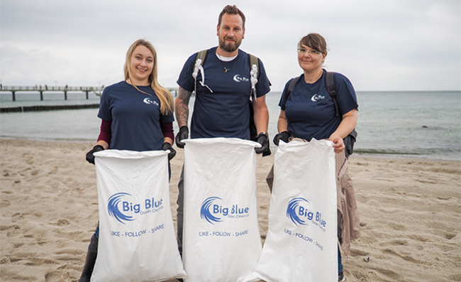 Tres empleados de Storopack en la playa con bolsas de basura