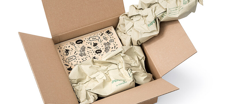 Una caja de cartón que contiene una caja de madera y tiras de almohadillados de papel de hierba