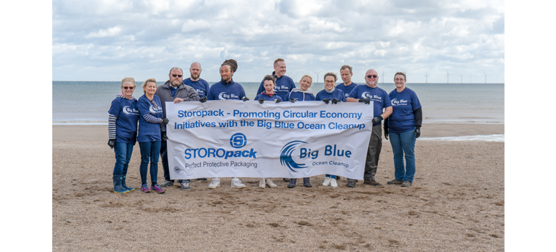 Varias personas posan para una foto de grupo en la playa sosteniendo una pancarta de Big Blue Ocean Cleanup